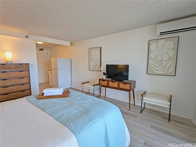 bedroom with a textured ceiling, light hardwood / wood-style floors, a wall mounted AC, and white fridge