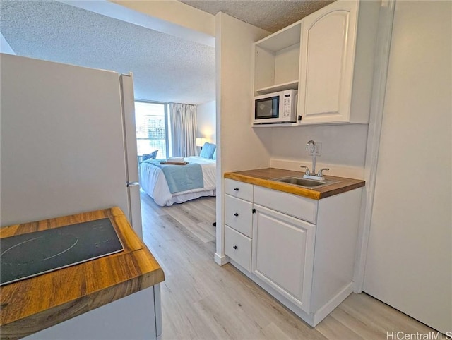 kitchen featuring white cabinetry, sink, a textured ceiling, and light hardwood / wood-style flooring