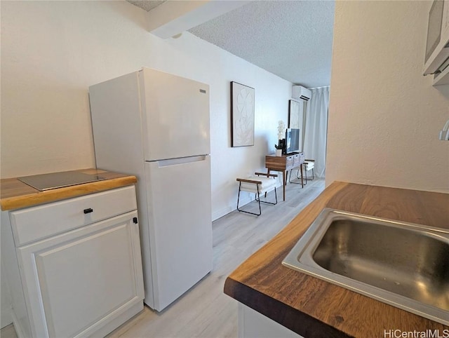 kitchen featuring light hardwood / wood-style flooring, an AC wall unit, white refrigerator, a textured ceiling, and white cabinets