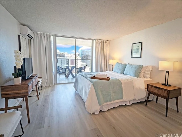 bedroom with a wall of windows, access to exterior, a textured ceiling, a wall unit AC, and light hardwood / wood-style flooring