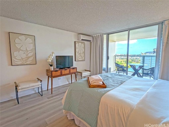 bedroom featuring hardwood / wood-style flooring, access to exterior, a wall unit AC, floor to ceiling windows, and a textured ceiling