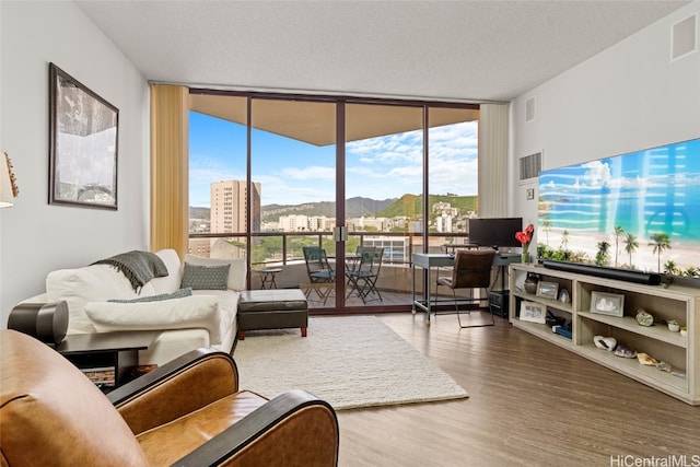 living room featuring wood-type flooring, a textured ceiling, and a wall of windows