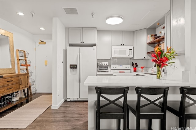 kitchen with dark hardwood / wood-style flooring, kitchen peninsula, a breakfast bar, and white appliances