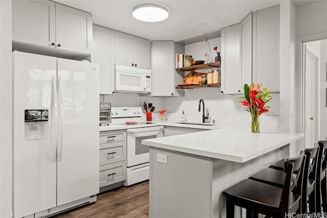 kitchen featuring kitchen peninsula, a kitchen bar, white appliances, dark wood-type flooring, and sink