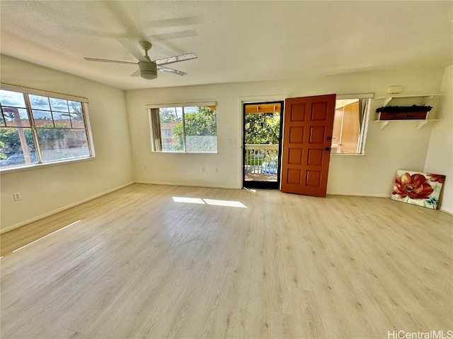 unfurnished room with ceiling fan, light wood-type flooring, a textured ceiling, and a wealth of natural light