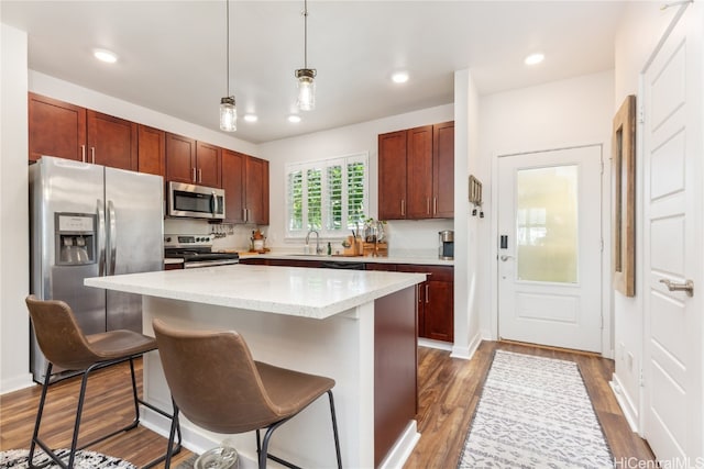 kitchen with a center island, a kitchen breakfast bar, dark hardwood / wood-style floors, appliances with stainless steel finishes, and decorative light fixtures