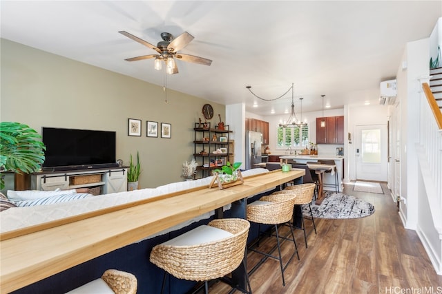 interior space featuring stainless steel refrigerator with ice dispenser, a kitchen breakfast bar, ceiling fan with notable chandelier, a wall unit AC, and wood-type flooring