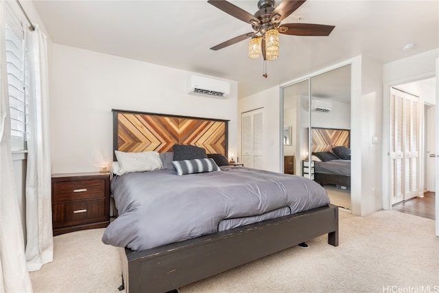 bedroom with light colored carpet, an AC wall unit, ceiling fan, and multiple closets