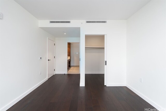 unfurnished bedroom featuring a walk in closet, dark hardwood / wood-style flooring, and a closet