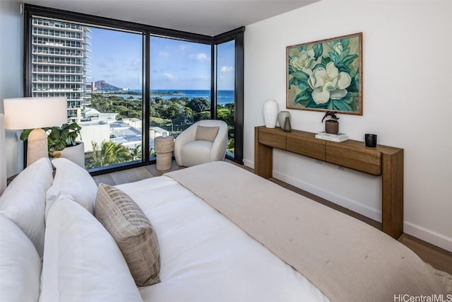 bedroom with hardwood / wood-style floors, a water view, and a wall of windows