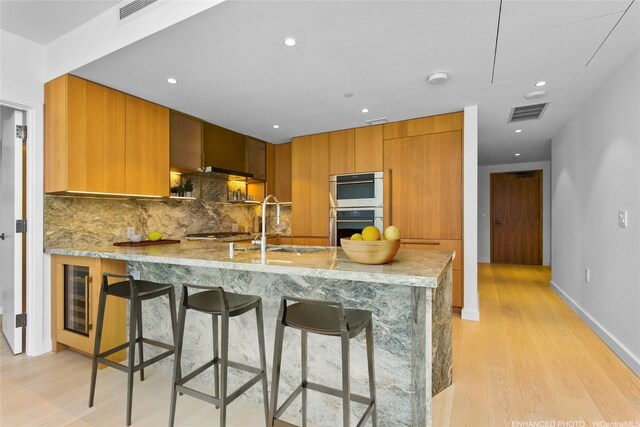 kitchen with beverage cooler, light hardwood / wood-style flooring, backsplash, kitchen peninsula, and appliances with stainless steel finishes