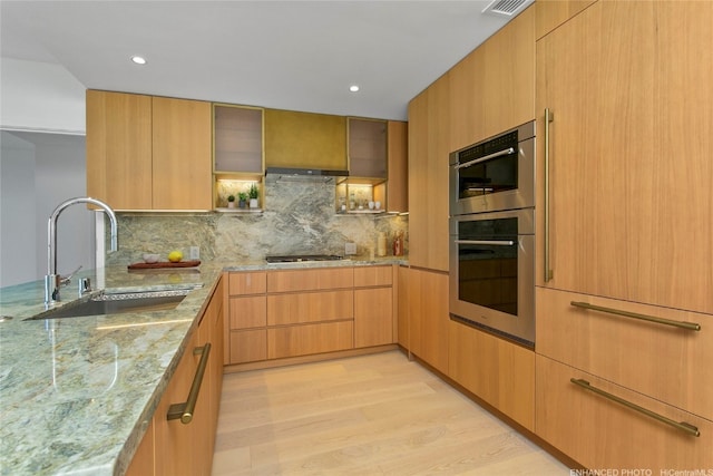 kitchen featuring tasteful backsplash, light stone countertops, sink, and light hardwood / wood-style floors