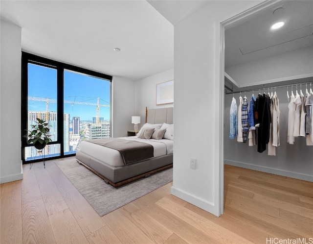 bedroom featuring access to exterior, a closet, light hardwood / wood-style flooring, and a wall of windows