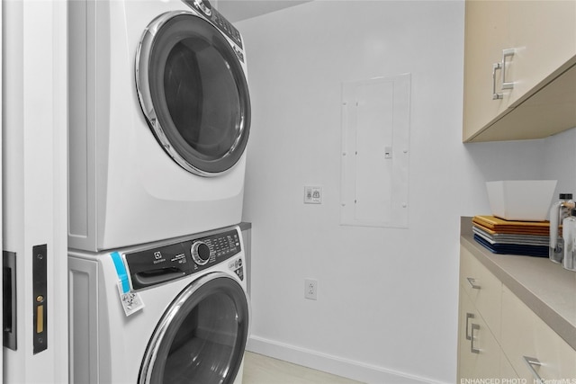 laundry room featuring cabinets, electric panel, and stacked washer and dryer