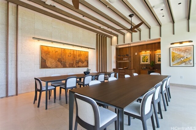 dining room featuring tile walls, wooden walls, beamed ceiling, and a high ceiling