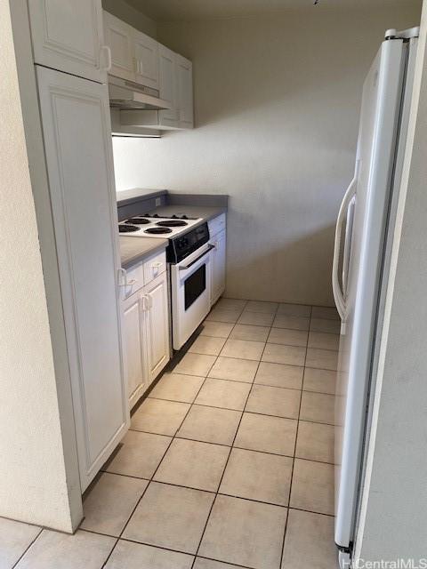 3054 Ala Poha Pl Unit 1906, Honolulu, HI 96818 - kitchen with white range with electric cooktop, freestanding refrigerator, under cabinet range hood, light tile patterned floors, and white cabinets