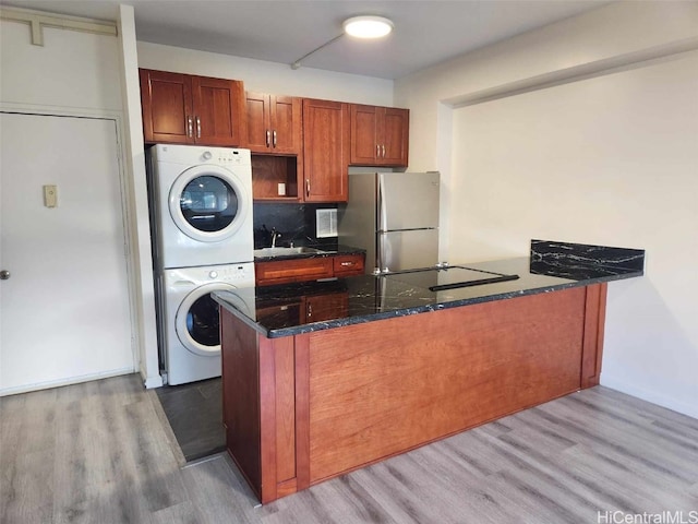 kitchen featuring kitchen peninsula, stainless steel fridge, sink, light hardwood / wood-style flooring, and stacked washer / drying machine