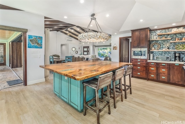 kitchen featuring stainless steel microwave, wooden counters, a chandelier, a kitchen island, and light wood-type flooring