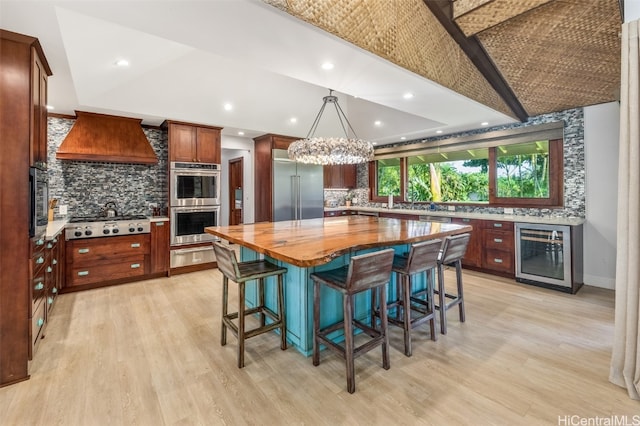 kitchen featuring wood counters, beverage cooler, built in appliances, decorative light fixtures, and a center island