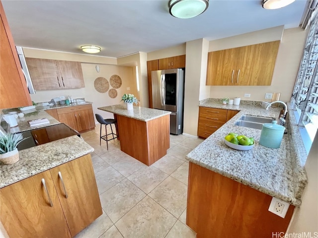 kitchen with stainless steel refrigerator, light stone countertops, sink, a breakfast bar area, and a kitchen island