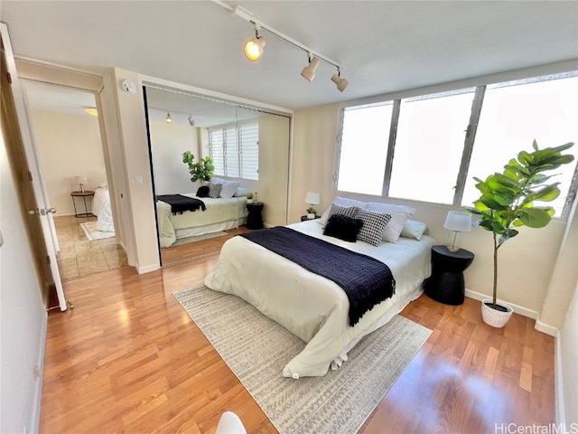 bedroom with light wood-type flooring, rail lighting, and a closet