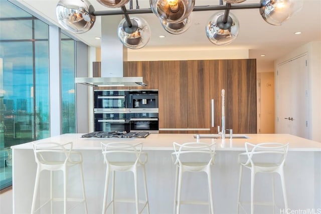 kitchen featuring double oven, ventilation hood, sink, and a kitchen breakfast bar