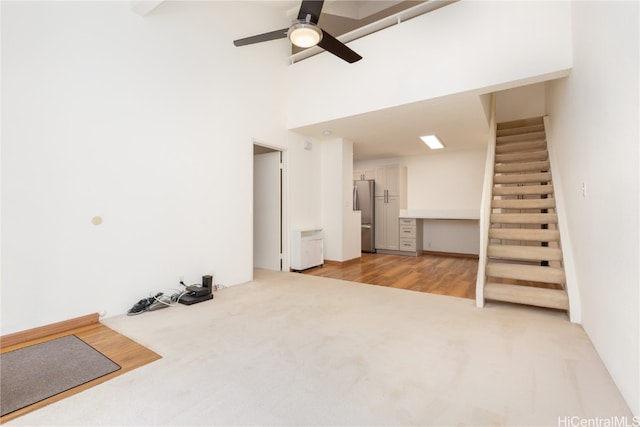 unfurnished living room featuring a high ceiling, light wood-type flooring, and ceiling fan