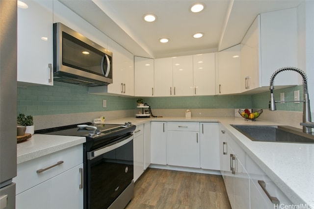 kitchen featuring sink, black range with electric cooktop, light stone counters, hardwood / wood-style floors, and white cabinets