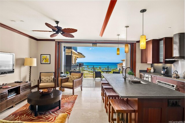 kitchen featuring wall chimney exhaust hood, a sink, dark countertops, a kitchen bar, and a ceiling fan