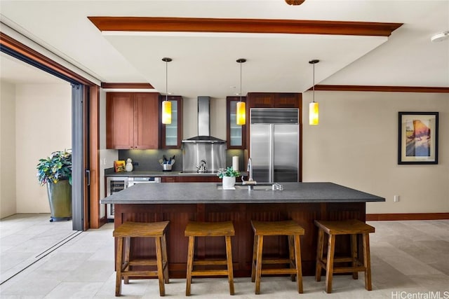 kitchen with stainless steel built in fridge, a kitchen breakfast bar, backsplash, dark countertops, and wall chimney range hood