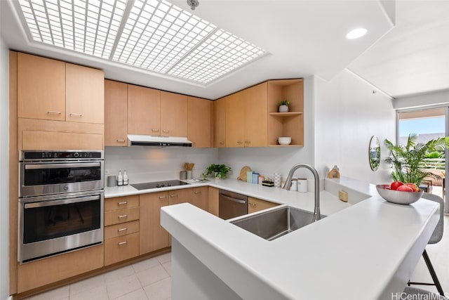 kitchen featuring a breakfast bar, light brown cabinets, sink, appliances with stainless steel finishes, and kitchen peninsula