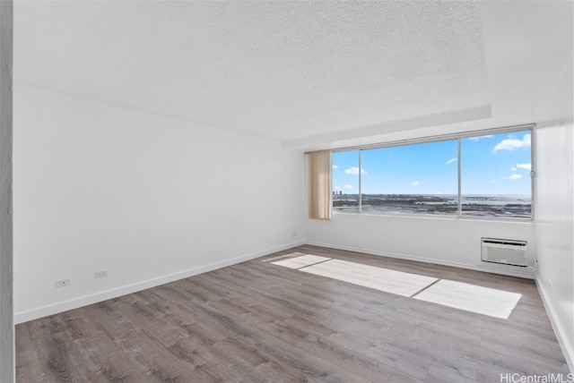 spare room featuring a wall mounted air conditioner, a textured ceiling, and light hardwood / wood-style flooring