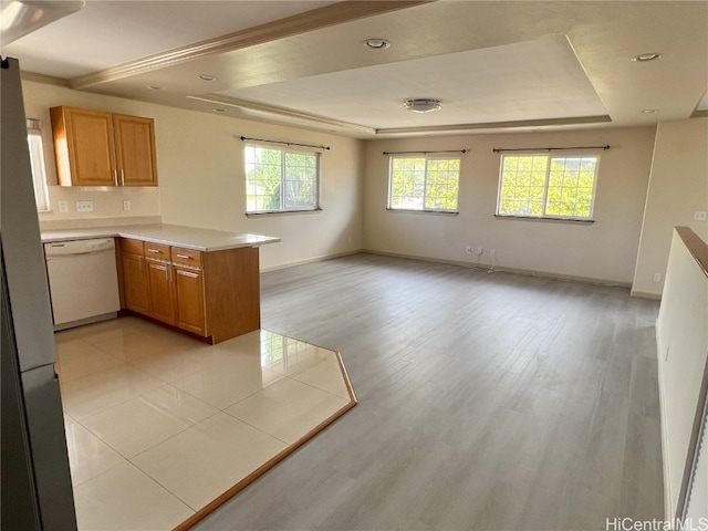 kitchen featuring white dishwasher, light wood-type flooring, kitchen peninsula, and a tray ceiling