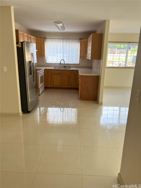 kitchen featuring white range oven, sink, light tile patterned flooring, and stainless steel refrigerator with ice dispenser