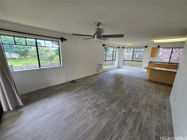 unfurnished living room featuring dark hardwood / wood-style flooring, a wall unit AC, plenty of natural light, and ceiling fan