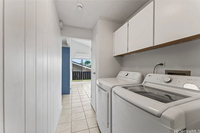 washroom featuring cabinets, a textured ceiling, washer and clothes dryer, wooden walls, and light tile patterned flooring