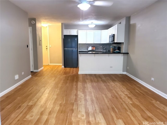 kitchen featuring white cabinetry, sink, black fridge, decorative backsplash, and light wood-type flooring