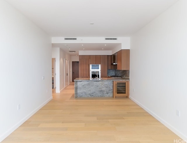 kitchen featuring decorative backsplash, light wood-type flooring, wine cooler, and wall chimney exhaust hood