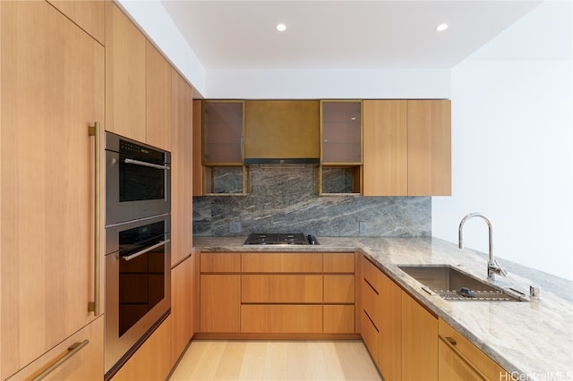 kitchen featuring gas cooktop, decorative backsplash, light wood-type flooring, light stone counters, and sink