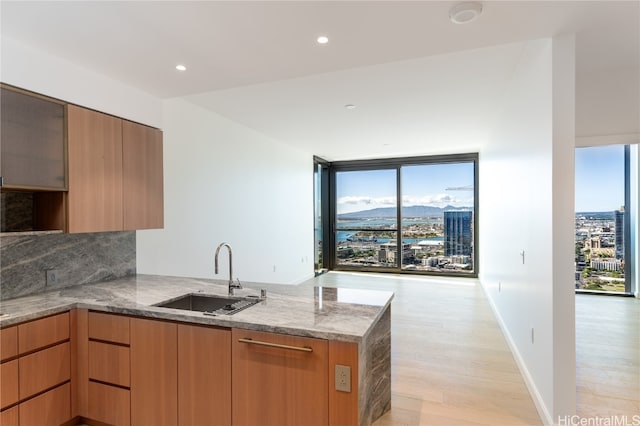 kitchen with light stone countertops, sink, backsplash, kitchen peninsula, and light wood-type flooring