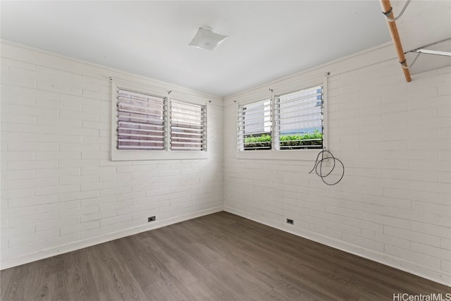 spare room featuring dark hardwood / wood-style floors and brick wall