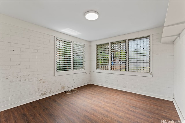 spare room featuring dark wood-type flooring and brick wall