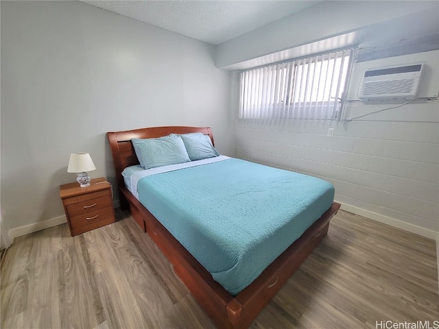 bedroom with hardwood / wood-style floors, a textured ceiling, and a wall mounted AC