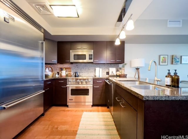 kitchen featuring high end appliances, sink, decorative backsplash, light wood-type flooring, and dark brown cabinetry