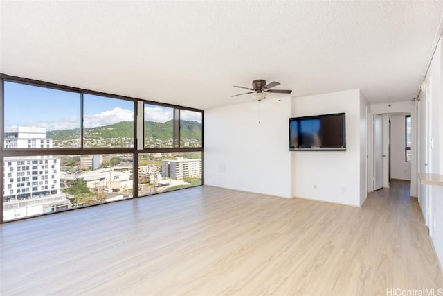 unfurnished living room with ceiling fan, light hardwood / wood-style flooring, expansive windows, and a textured ceiling