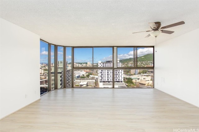 spare room with ceiling fan, a wall of windows, a textured ceiling, and light hardwood / wood-style flooring