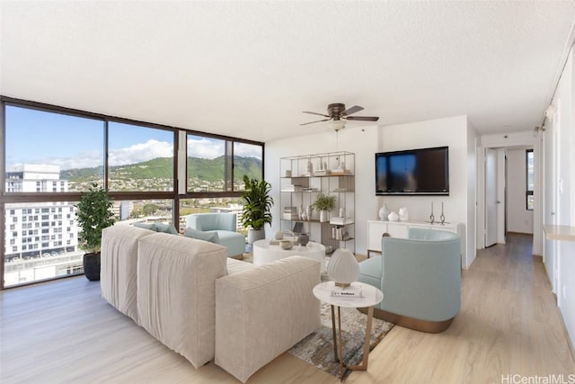 living room featuring ceiling fan, floor to ceiling windows, light hardwood / wood-style floors, and a textured ceiling