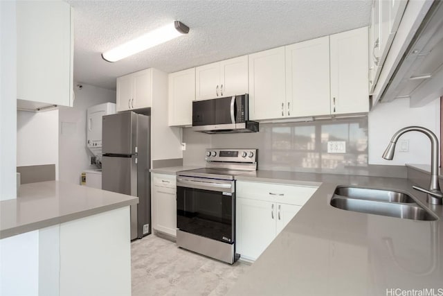 kitchen featuring appliances with stainless steel finishes, a textured ceiling, sink, stacked washer and clothes dryer, and white cabinetry