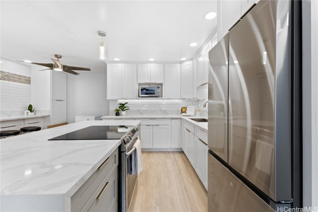 kitchen featuring decorative backsplash, stainless steel appliances, light hardwood / wood-style floors, white cabinetry, and hanging light fixtures