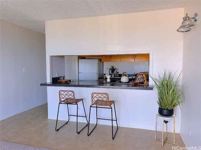 kitchen with a breakfast bar, white refrigerator, kitchen peninsula, and a textured ceiling